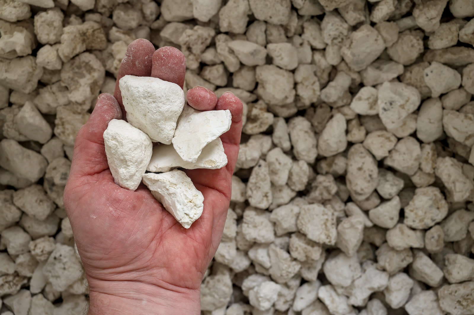 Hand holding raw magnesite ore over a stockpile